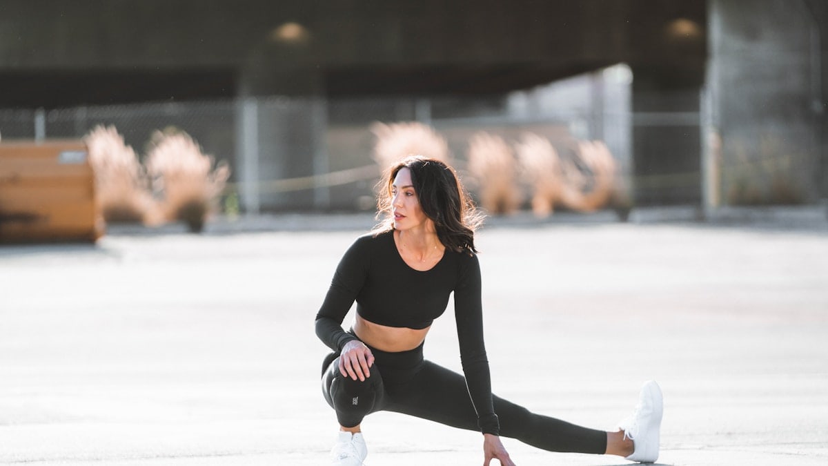 woman in black tank top and black leggings holding black and white nike shoes